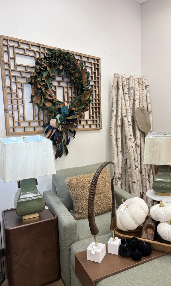 A sage armchair between green lamps, under a magnolia wreath on a wooden lattice screen